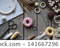 Flat lay knitting and crochet workspace with colorful donut shaped pincushions embroidery hoop scissors yarn lace and sewing accessories on rustic wooden background with copy space 141667296