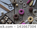 Sewing and knitting tools flat lay with donut pincushions embroidery hoop scissors yarn beads and lace on rustic wooden table cozy handmade craft background 141667304