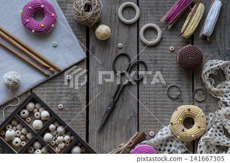 Handmade sewing and knitting workspace with colorful pincushions embroidery hoop lace scissors yarn and crochet accessories on wooden background flat lay style Handmade sewing and knitting workspace with colorful pincushions embroidery hoop lace scissors yarn and crochet accessories on wooden background flat lay style 141667305