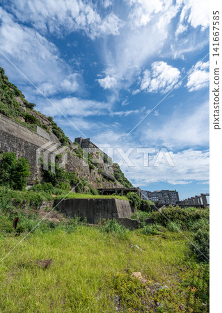 Concrete apartments and retaining walls of Gunkanjima as seen from a green grassy area. Concrete apartments and retaining walls of Gunkanjima as seen from a green grassy area. 141667585
