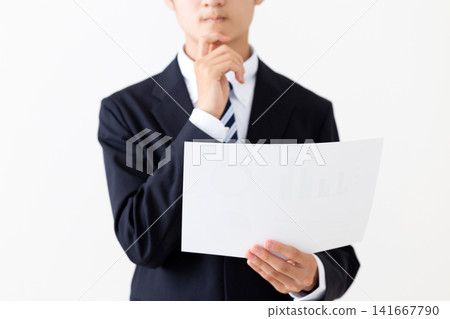 A young businessman in a suit is shown holding graphs and looking troubled. A young businessman in a suit is shown holding graphs and looking troubled. 141667790