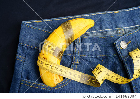 Banana with measuring tape on jean trousers, penis health. Banana with measuring tape on jean trousers, penis health. 141668394