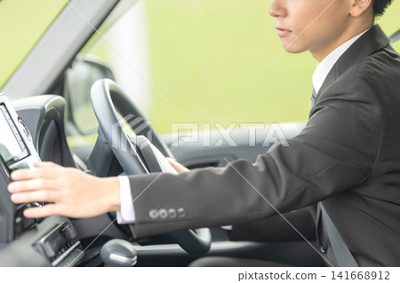 A businessman operating a car navigation system; an image of him checking something while driving. A businessman operating a car navigation system; an image of him checking something while driving. 141668912