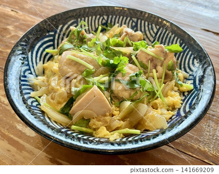 A homemade oyakodon (chicken and egg rice bowl) with plenty of mitsuba (Japanese parsley) placed on a wooden table. A homemade oyakodon (chicken and egg rice bowl) with plenty of mitsuba (Japanese parsley) placed on a wooden table. 141669209