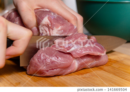 Hands cutting fresh raw meat on wooden board photo Hands cutting fresh raw meat on wooden board photo 141669504