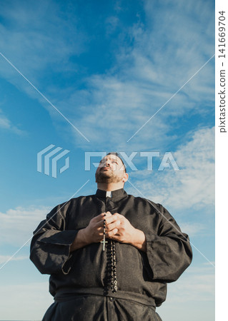 Monk Praying With The Crucifix Under The Clear Blue Sky Monk Praying With The Crucifix Under The Clear Blue Sky 141669704