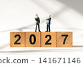 Miniature Businessmen Standing on Wooden 2027 Blocks Discussing Future Business Strategy 141671146