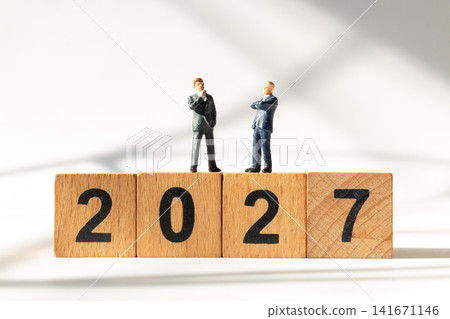 Miniature Businessmen Standing on Wooden 2027 Blocks Discussing Future Business Strategy Miniature Businessmen Standing on Wooden 2027 Blocks Discussing Future Business Strategy 141671146