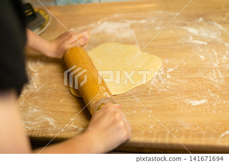 Rolling out dough with wooden pin close up photo Rolling out dough with wooden pin close up photo 141671694