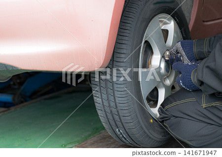 Hands tightening a car tire with a tool; an image of car maintenance. Hands tightening a car tire with a tool; an image of car maintenance. 141671947