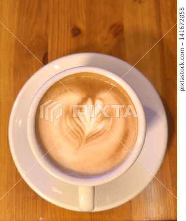 A cup of aromatic cappuccino with latte art on top, top-down view on a wooden table. 141672858