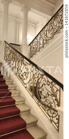 A magnificent grand staircase with wrought-iron railings and a red carpet. A magnificent grand staircase with wrought-iron railings and a red carpet. 141672859