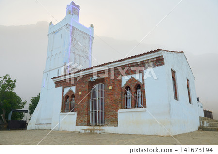 White mosque tower and brick building in misty mountain village at dawn 141673194