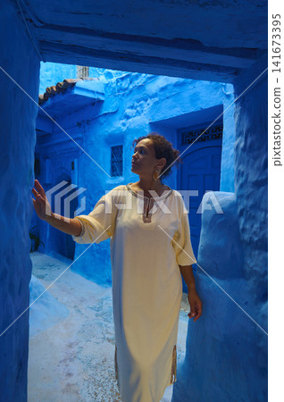 Woman exploring the blue alleys of Chefchaouen in a white traditional dress Woman exploring the blue alleys of Chefchaouen in a white traditional dress 141673395