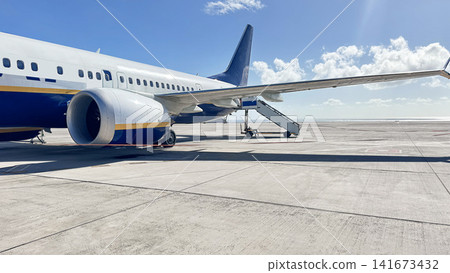 Commercial passenger aircraft waits on the airport apron with boarding stairs beside the fuselage under a clear blue sky. Air travel, aviation, transportation, departures and tourism. Commercial passenger aircraft waits on the airport apron with boarding stairs beside the fuselage under a clear blue sky. Air travel, aviation, transportation, departures and tourism. 141673432