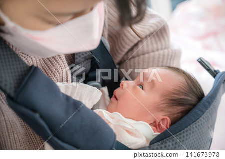 A parent holding a baby in a baby carrier; an image of childcare. A parent holding a baby in a baby carrier; an image of childcare. 141673978
