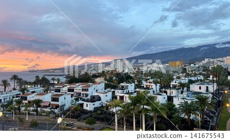 Scenic view of a Tenerife resort town with palm trees modern hotels and mountain landscape at sunset. Popular travel destination in the Canary Islands known for tourism beach holidays surfing vacation Scenic view of a Tenerife resort town with palm trees modern hotels and mountain landscape at sunset. Popular travel destination in the Canary Islands known for tourism beach holidays surfing vacation 141675543