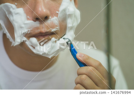 A 40-year-old man's morning shave: shaving his chin with a T-shaped razor after applying plenty of shaving foam. A 40-year-old man's morning shave: shaving his chin with a T-shaped razor after applying plenty of shaving foam. 141676994