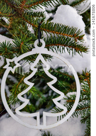 A decorated Christmas tree stands covered in snow. The scene shows a metal ornament shaped like a tree hanging from the branches in a winter setting 141678806