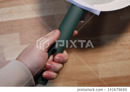 Hand Holding Green Tool Handle on Wooden Surface 141679688