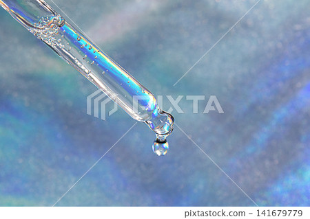 Close-up of a pipette dropper releasing a serum droplet over iridescent blue background Close-up of a pipette dropper releasing a serum droplet over iridescent blue background 141679779