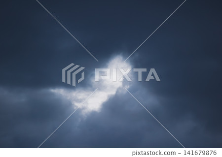 Dramatic dark storm cloud background with light glowing through a center gap Dramatic dark storm cloud background with light glowing through a center gap 141679876