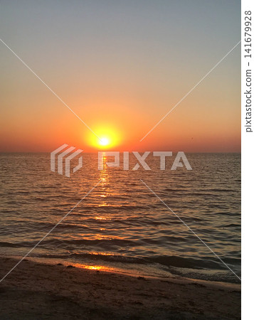 Warm sunrise above the sea with a bright reflection path on gentle waves and a sandy beach in the foreground. Minimal, serene seascape with clean copy space for travel, wellness, banner or background Warm sunrise above the sea with a bright reflection path on gentle waves and a sandy beach in the foreground. Minimal, serene seascape with clean copy space for travel, wellness, banner or background 141679928