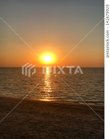 Warm sunrise above the sea with a bright reflection path on gentle waves and a sandy beach in the foreground. Minimal, serene seascape with clean copy space for travel, wellness, banner or background Warm sunrise above the sea with a bright reflection path on gentle waves and a sandy beach in the foreground. Minimal, serene seascape with clean copy space for travel, wellness, banner or background 141679929