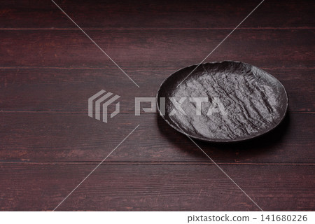 An empty round ceramic plate on a dark, textured brown background. An empty round plate An empty round ceramic plate on a dark, textured brown background. An empty round plate 141680226