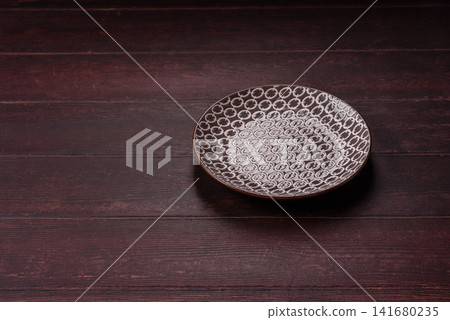 An empty round ceramic plate on a dark, textured brown background. An empty round plate An empty round ceramic plate on a dark, textured brown background. An empty round plate 141680235