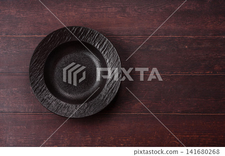 An empty round ceramic plate on a dark, textured brown background. An empty round plate An empty round ceramic plate on a dark, textured brown background. An empty round plate 141680268