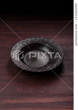 An empty round ceramic plate on a dark, textured brown background. An empty round plate An empty round ceramic plate on a dark, textured brown background. An empty round plate 141680269