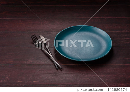 An empty round ceramic plate on a dark, textured brown background. An empty round plate An empty round ceramic plate on a dark, textured brown background. An empty round plate 141680274