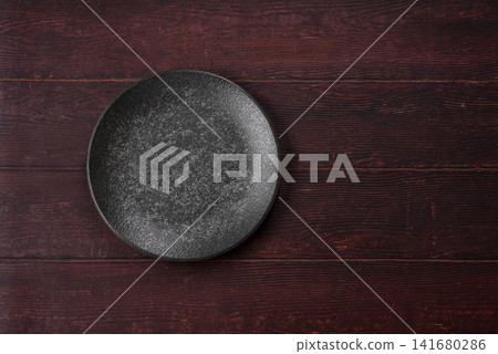 An empty round ceramic plate on a dark, textured brown background. An empty round plate An empty round ceramic plate on a dark, textured brown background. An empty round plate 141680286