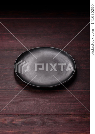 An empty round ceramic plate on a dark, textured brown background. An empty round plate An empty round ceramic plate on a dark, textured brown background. An empty round plate 141680290