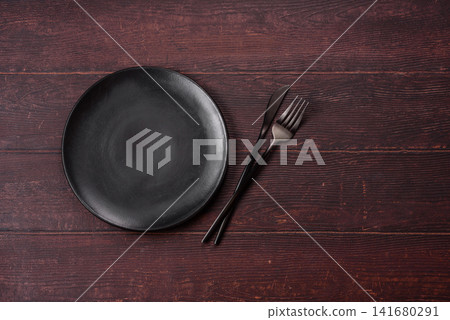 An empty round ceramic plate on a dark, textured brown background. An empty round plate An empty round ceramic plate on a dark, textured brown background. An empty round plate 141680291