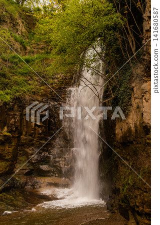 Majestic Waterfall Cascading Down a Steep Rocky Cliff Surrounded by Lush Green Vegetation and Fores Majestic Waterfall Cascading Down a Steep Rocky Cliff Surrounded by Lush Green Vegetation and Fores 141680587