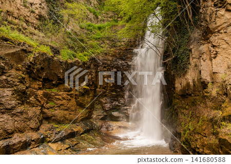 Majestic Waterfall Cascading Down a Steep Rocky Cliff Surrounded by Lush Green Vegetation and Fores Majestic Waterfall Cascading Down a Steep Rocky Cliff Surrounded by Lush Green Vegetation and Fores 141680588