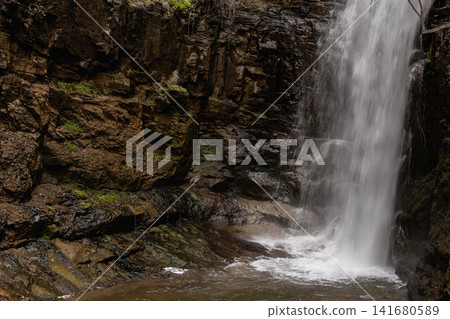 Majestic Waterfall Cascading Down a Steep Rocky Cliff Surrounded by Lush Green Vegetation and Fores Majestic Waterfall Cascading Down a Steep Rocky Cliff Surrounded by Lush Green Vegetation and Fores 141680589