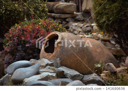 Ancient Clay Amphora Resting Near Weathered Log in Rustic Garden Landscape Historic Pottery Artifac 141680636
