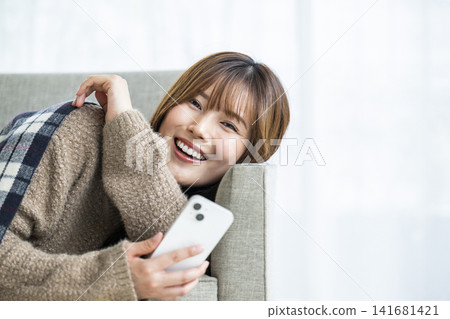 在房間裡操作智慧型手機的年輕女子 在房間裡操作智慧型手機的年輕女子 141681421