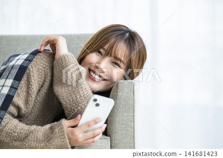 在房間裡操作智慧型手機的年輕女子 在房間裡操作智慧型手機的年輕女子 141681423
