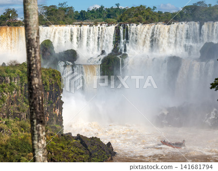 A magnificent panoramic view of Iguazu Falls and a Macco Safari boat heading towards the base of the falls. A magnificent panoramic view of Iguazu Falls and a Macco Safari boat heading towards the base of the falls. 141681794