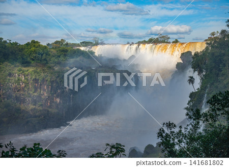 The Iguazu Valley is filled with mist as the sun shines on the ridge of the waterfall. The Iguazu Valley is filled with mist as the sun shines on the ridge of the waterfall. 141681802