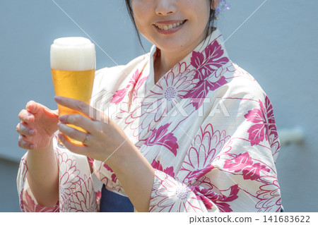 A beautiful woman in a yukata holds up a beer against a blue sky. A beautiful woman in a yukata holds up a beer against a blue sky. 141683622