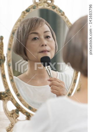 一位老年婦女在鏡子前化妝。 一位老年婦女在鏡子前化妝。 141683796