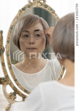Senior woman applying makeup in front of a mirror Senior woman applying makeup in front of a mirror 141683799