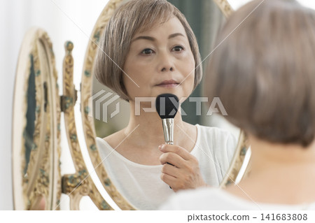 一位老年婦女在鏡子前化妝。 一位老年婦女在鏡子前化妝。 141683808