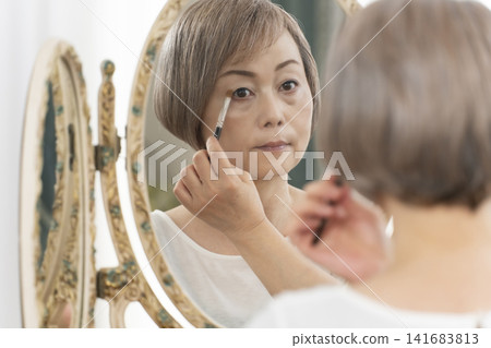 一位老年婦女在鏡子前化妝。 一位老年婦女在鏡子前化妝。 141683813