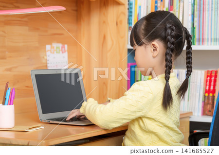 Asian little girl using laptop at wooden desk, back view child learning at home, online education concept Asian little girl using laptop at wooden desk, back view child learning at home, online education concept 141685527